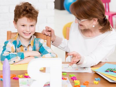 Happy little boy with mental disorder having private reading lesson with children therapist